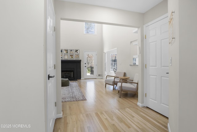 entrance foyer featuring light wood finished floors, a fireplace with flush hearth, a high ceiling, and baseboards