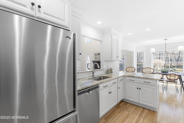 kitchen with light stone counters, light wood-style flooring, stainless steel appliances, a sink, and decorative backsplash