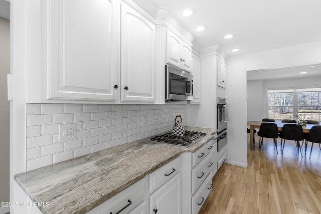 kitchen featuring decorative backsplash, appliances with stainless steel finishes, light wood-style floors, white cabinetry, and light stone countertops