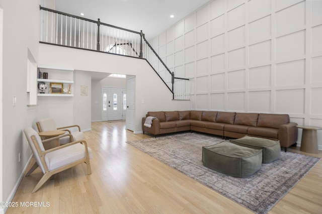 living area with a decorative wall, wood finished floors, a towering ceiling, baseboards, and stairway