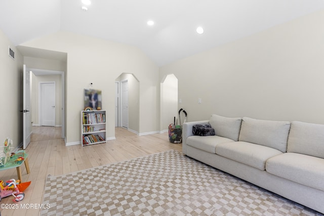 living area with arched walkways, lofted ceiling, visible vents, light wood-style floors, and baseboards