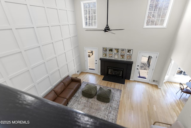 living area featuring a fireplace, a decorative wall, a high ceiling, ceiling fan, and wood finished floors