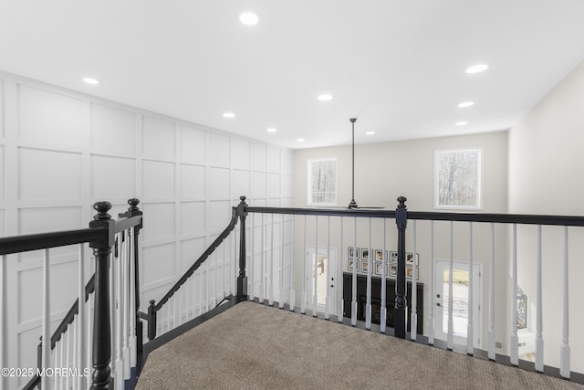 hallway with recessed lighting, a decorative wall, a wealth of natural light, and an upstairs landing