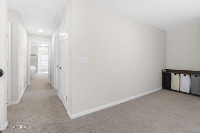 hall with attic access, light colored carpet, and baseboards