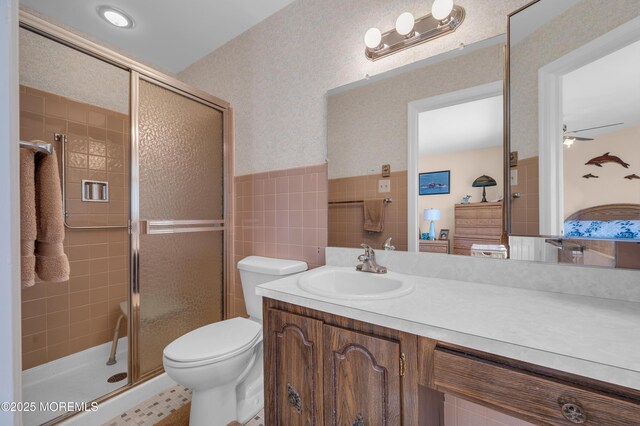 full bath with toilet, a ceiling fan, vanity, a shower stall, and wallpapered walls