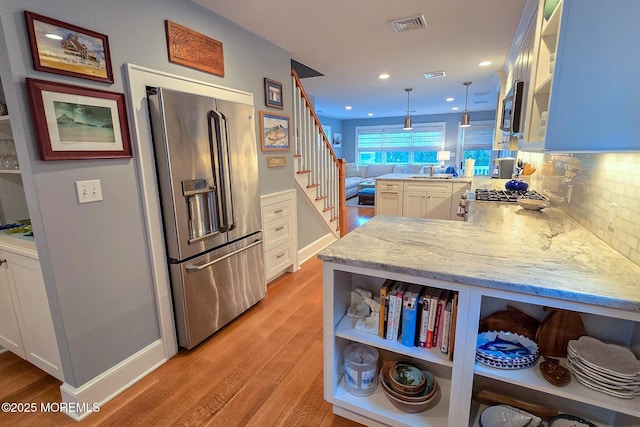 kitchen featuring light stone counters, visible vents, a peninsula, open shelves, and stainless steel appliances