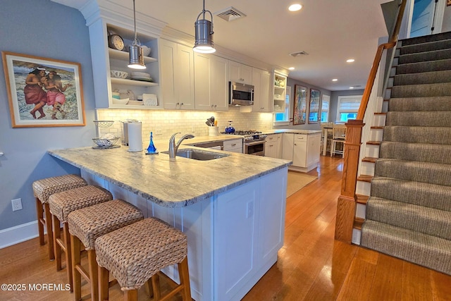 kitchen featuring visible vents, a sink, a peninsula, stainless steel appliances, and open shelves