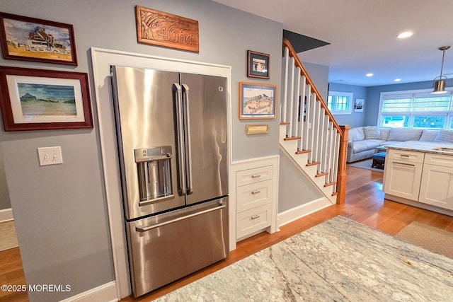 kitchen with light wood finished floors, light stone countertops, stainless steel fridge with ice dispenser, open floor plan, and white cabinetry