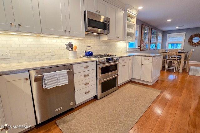 kitchen with light wood finished floors, white cabinets, stainless steel appliances, and tasteful backsplash