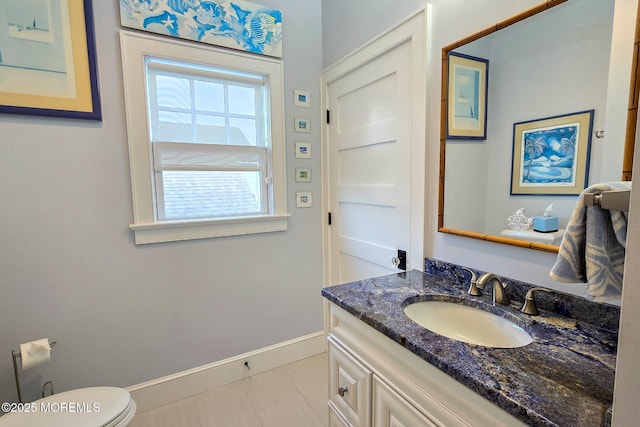 half bath with baseboards, toilet, and vanity