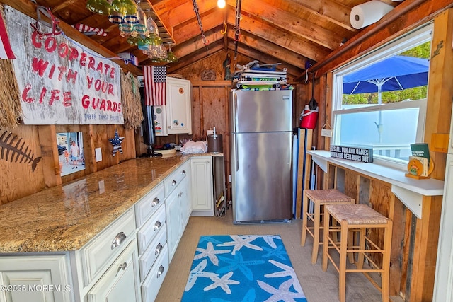 kitchen with wooden walls, vaulted ceiling, wooden ceiling, freestanding refrigerator, and white cabinets