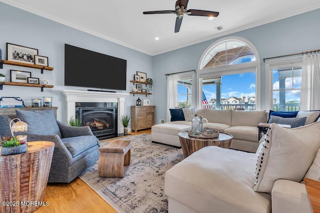 living room with wood finished floors, recessed lighting, ceiling fan, a glass covered fireplace, and crown molding