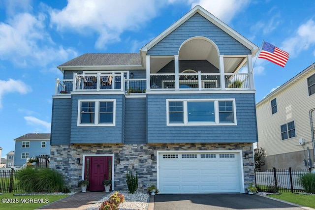 view of front of property featuring aphalt driveway, stone siding, a balcony, and fence