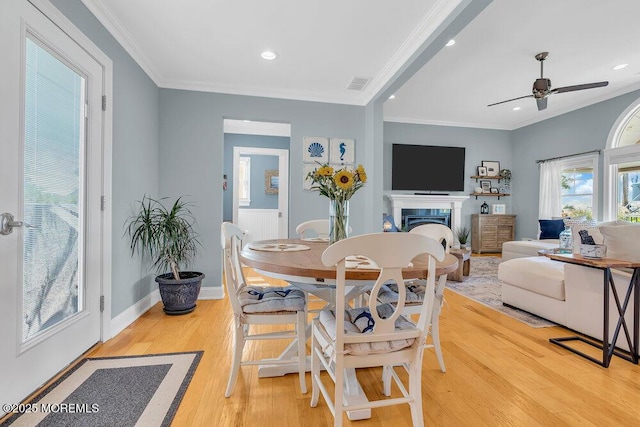 dining space featuring visible vents, ornamental molding, a fireplace, light wood finished floors, and baseboards