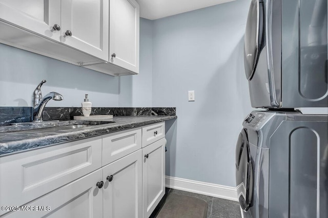 clothes washing area with baseboards, dark tile patterned floors, stacked washer and clothes dryer, cabinet space, and a sink