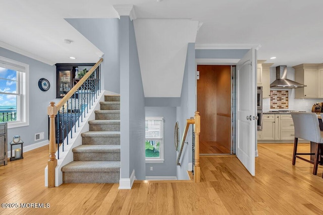 staircase featuring baseboards, wood finished floors, visible vents, and ornamental molding