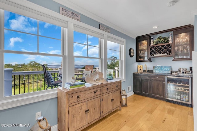 bar with a wealth of natural light, ornamental molding, wine cooler, light wood finished floors, and indoor wet bar