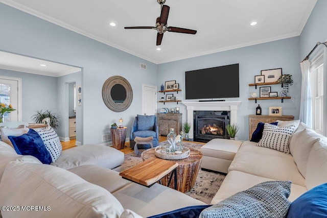 living area featuring a lit fireplace, a healthy amount of sunlight, and ornamental molding