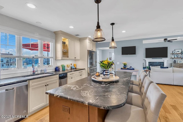 kitchen featuring a kitchen bar, light wood-style flooring, stainless steel appliances, a fireplace, and glass insert cabinets