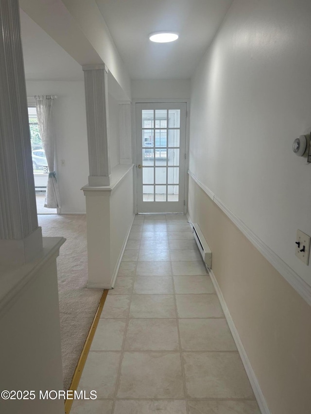 hallway with a baseboard radiator, light colored carpet, baseboards, and decorative columns