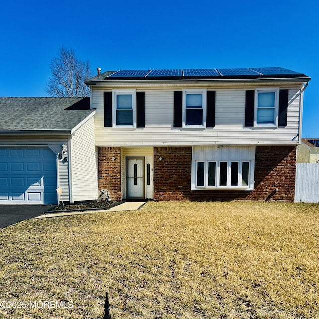 view of front facade with a front yard, fence, solar panels, an attached garage, and brick siding