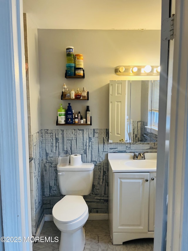 half bathroom with vanity, wainscoting, tile walls, toilet, and marble finish floor
