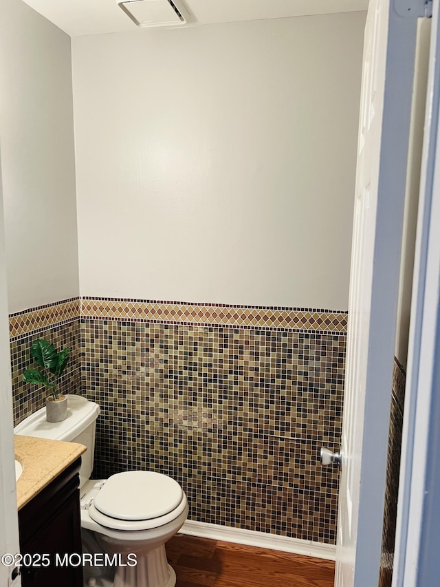 half bath featuring visible vents, tile walls, toilet, wood finished floors, and vanity