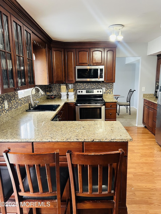 kitchen featuring a sink, light stone counters, stainless steel appliances, light wood-style floors, and decorative backsplash