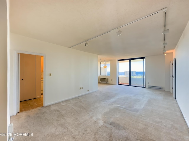 spare room featuring a wall mounted AC, baseboard heating, track lighting, and light colored carpet