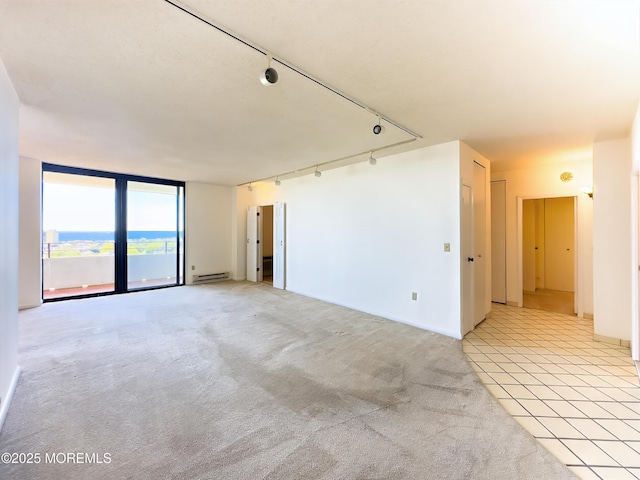 unfurnished room featuring floor to ceiling windows, light tile patterned floors, light colored carpet, baseboard heating, and track lighting