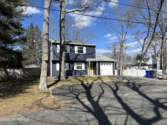 colonial inspired home featuring an attached garage, driveway, and fence