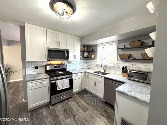 kitchen with stainless steel appliances, a sink, backsplash, light stone countertops, and open shelves