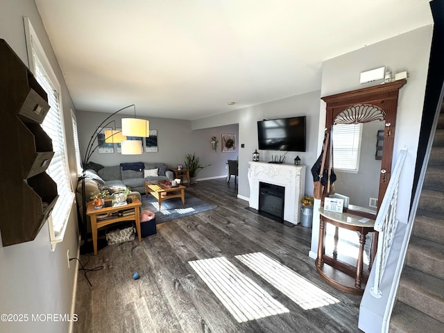 living area with a glass covered fireplace, stairway, wood finished floors, and baseboards