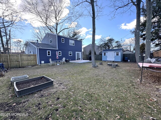 back of house with an outbuilding, a fenced backyard, a vegetable garden, and an outdoor fire pit