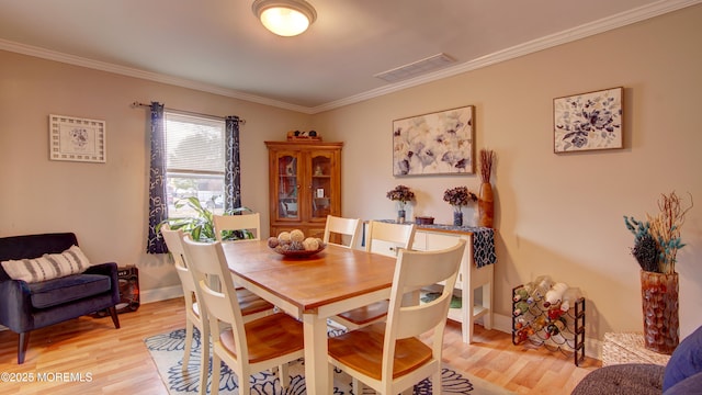 dining area with ornamental molding, light wood-type flooring, visible vents, and baseboards