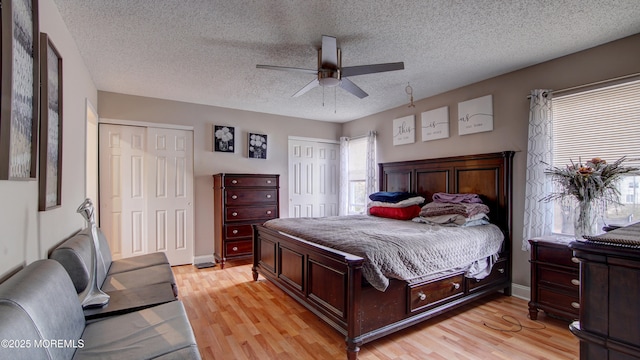 bedroom featuring multiple closets, ceiling fan, light wood-style flooring, and a textured ceiling