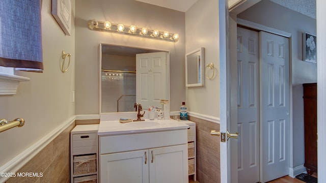 bathroom featuring a textured ceiling, vanity, tile walls, a shower, and wainscoting