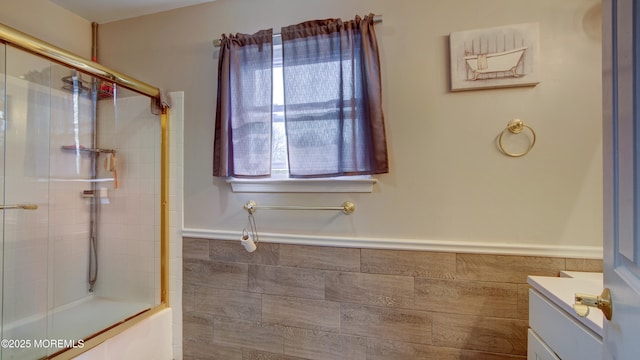 full bathroom featuring tile walls, a wainscoted wall, vanity, and bath / shower combo with glass door