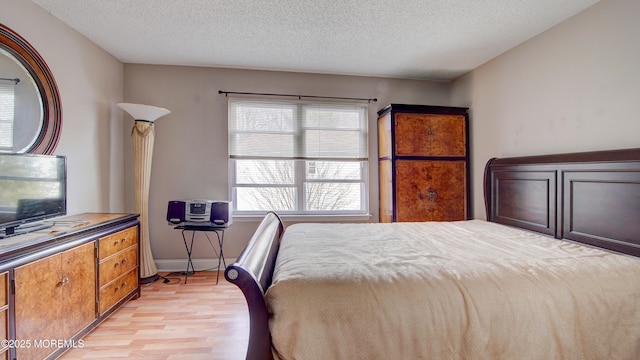 bedroom with light wood-style flooring, baseboards, and a textured ceiling