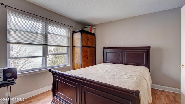 bedroom with light wood-style floors, a textured ceiling, and baseboards