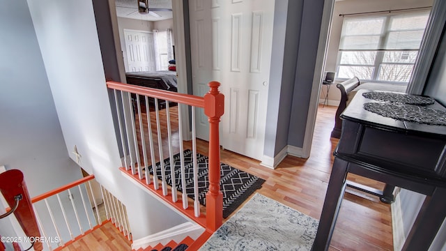 hallway featuring baseboards, wood finished floors, and an upstairs landing