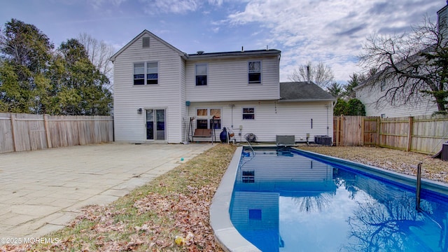 back of property with central AC, a patio area, a fenced backyard, and a fenced in pool