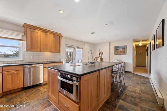 kitchen with dark countertops, stainless steel appliances, a baseboard radiator, and stone tile flooring