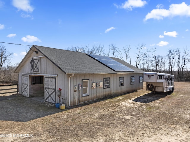 view of front of house featuring a garage, solar panels, roof with shingles, and an outdoor structure