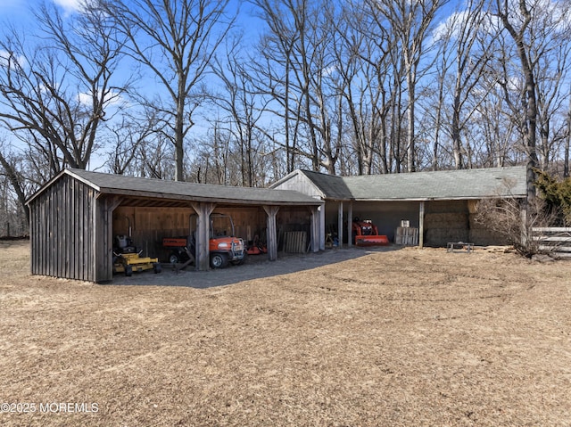 exterior space with a carport, a pole building, a shingled roof, and dirt driveway