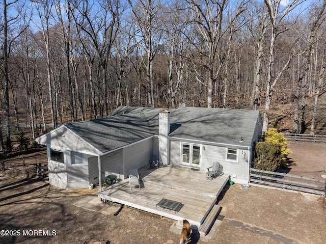 view of front of house featuring a chimney, fence, a deck, and a view of trees