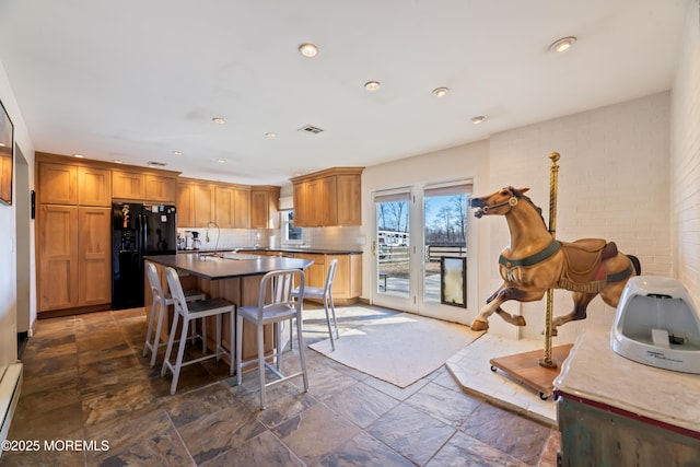 kitchen with decorative backsplash, a kitchen island, a breakfast bar area, baseboard heating, and black fridge