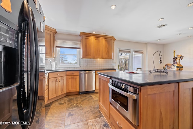 kitchen featuring stainless steel appliances, a sink, visible vents, decorative backsplash, and dark countertops