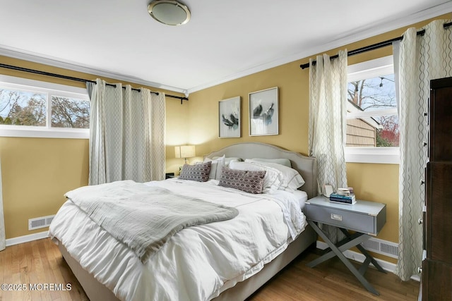 bedroom with visible vents, crown molding, baseboards, and wood finished floors