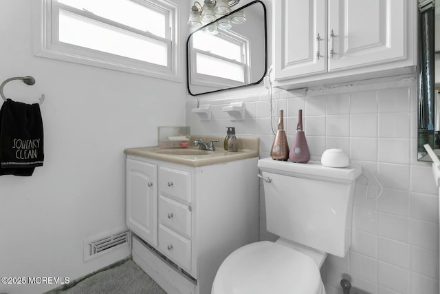 half bath featuring visible vents, toilet, tile walls, and vanity